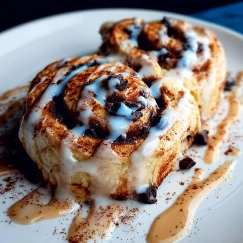 Delicious chocolate cookie cinnamon rolls drizzled with icing and topped with chocolate chips.